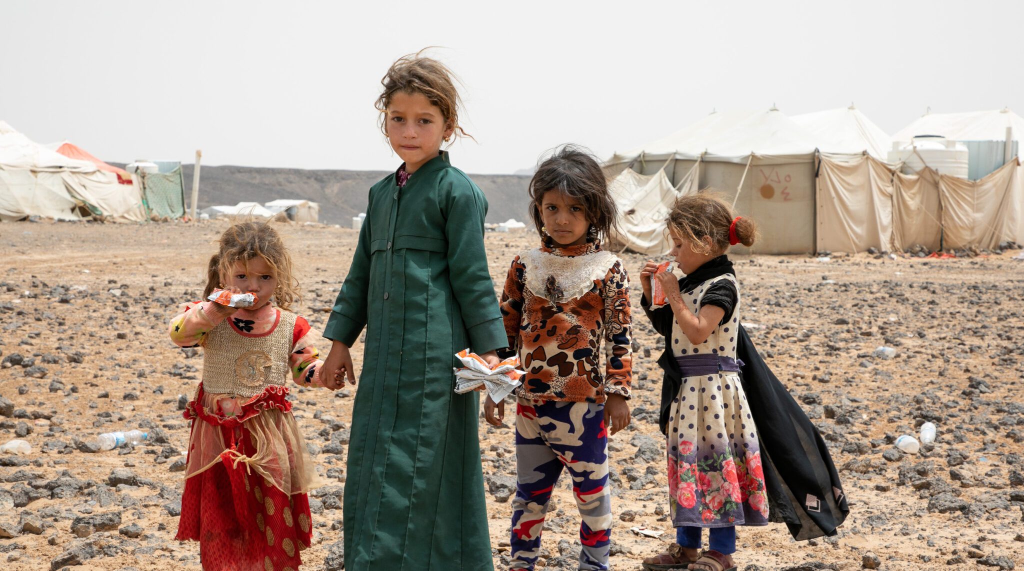 An image of children standing in a desert landscape with tents in the background.